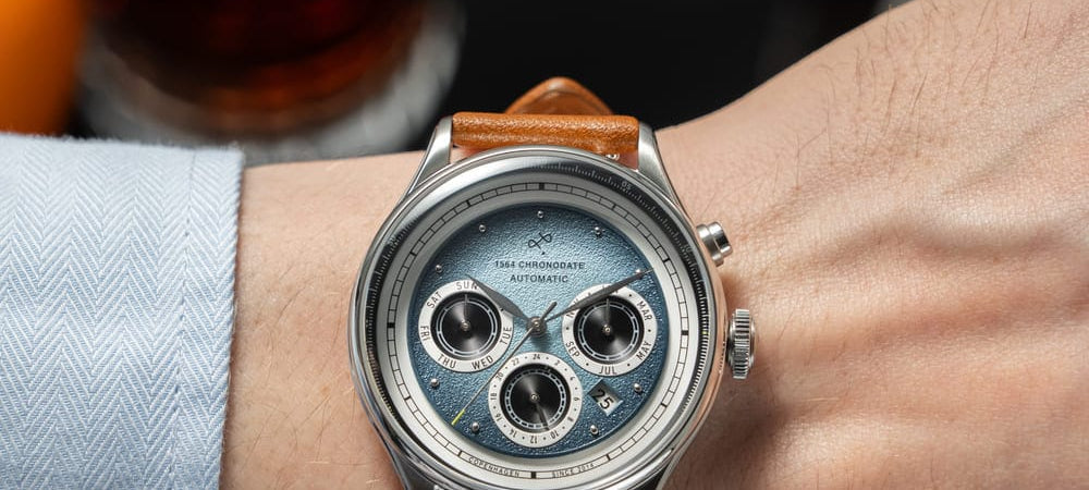 A chronograph watch on a leather strap worn at a bar, with a shirt cuff and a negroni in frame