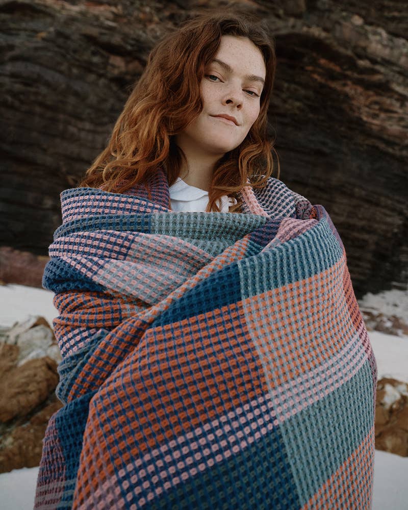 A woman wrapped in a Mungo Vrou-Vrou blanket outdoors, showing the waffle texture and weight
