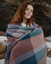 A woman wrapped in a Mungo Vrou-Vrou blanket outdoors, showing the waffle texture and weight