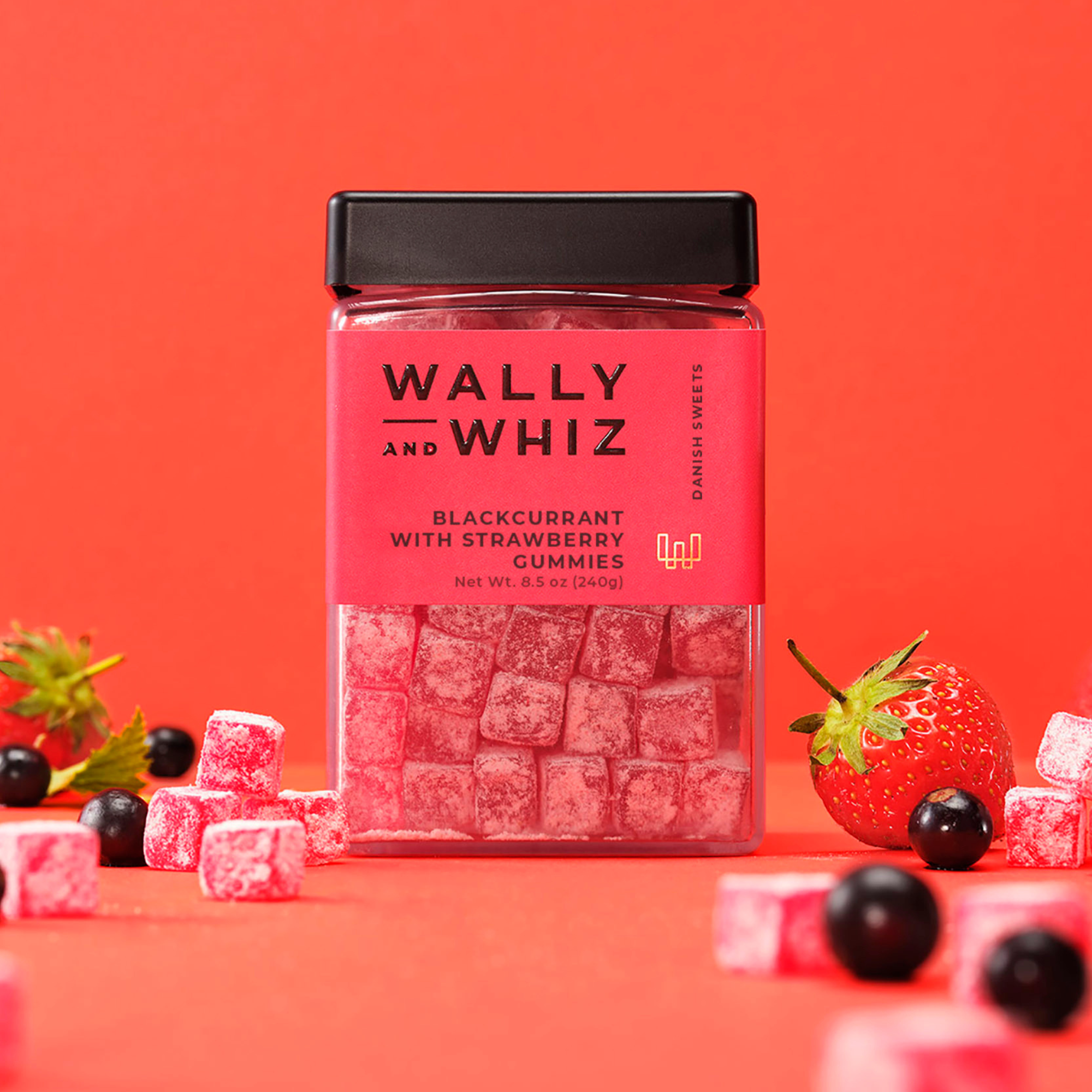 Wally and Whiz blackcurrant with strawberry gummies in a red 8.5 oz jar, surrounded by strawberries and blackcurrants