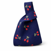 The navy cherry knitted bag with its handles knotted, carried as a handheld pouch