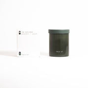 The Explorer Candle in a dark green glass jar with its printed box