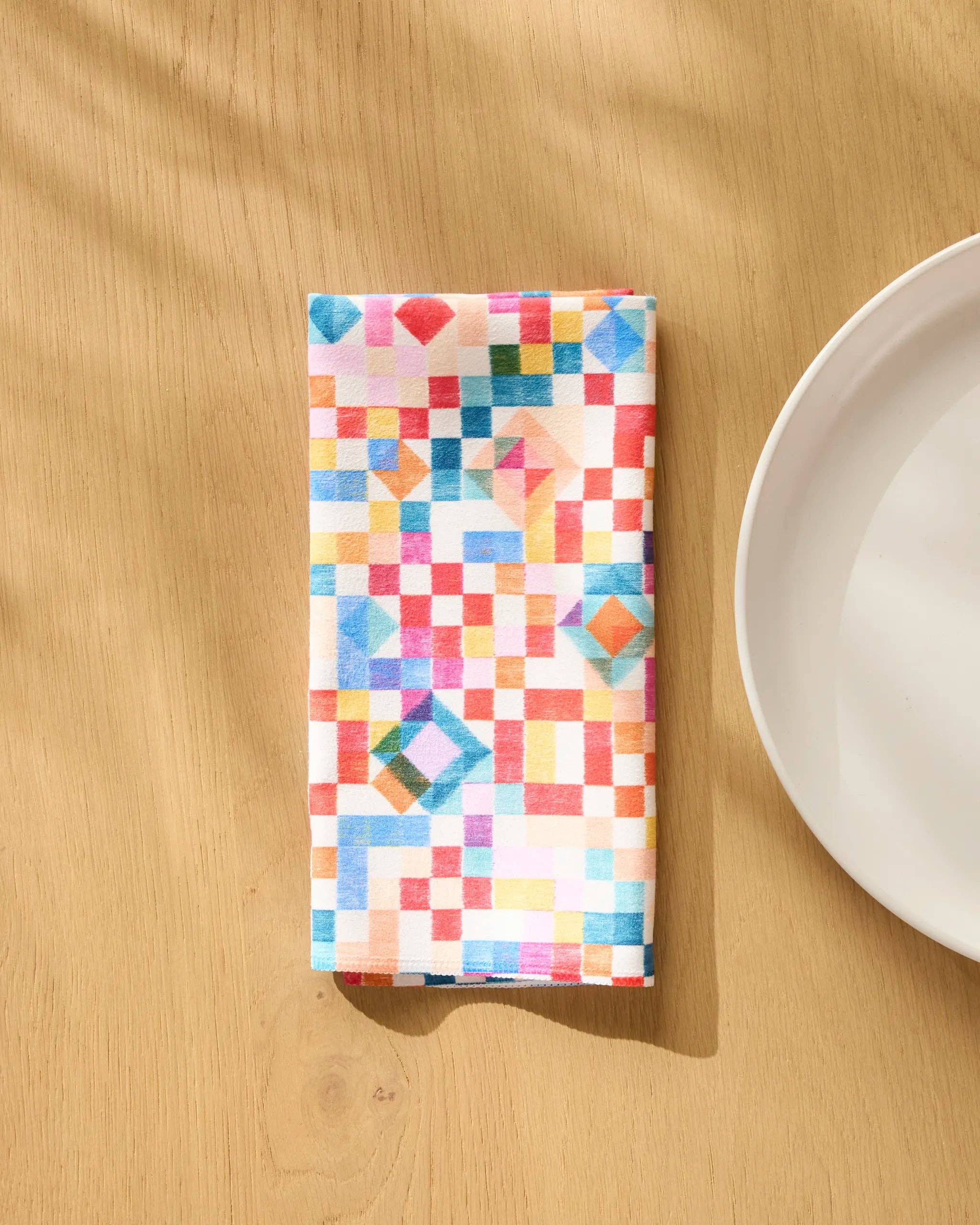Patchwork Geo napkin folded on a wooden table beside a white plate