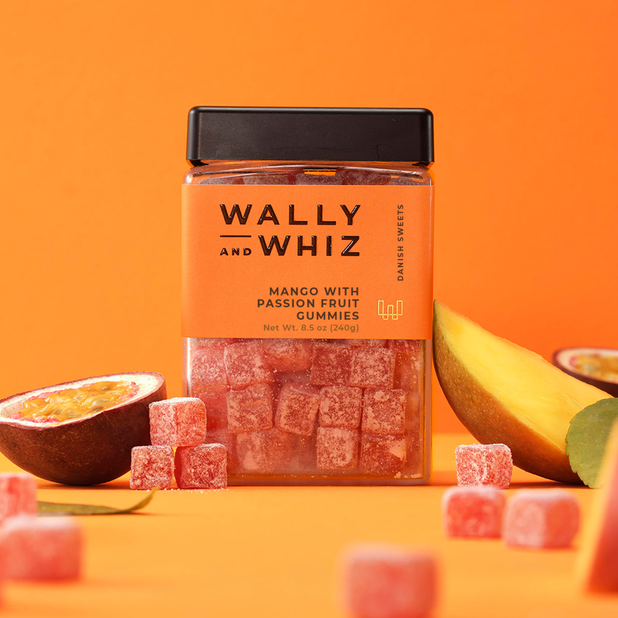 Wally and Whiz mango with passion fruit gummies in an orange 8.5 oz jar, surrounded by mango and passion fruit