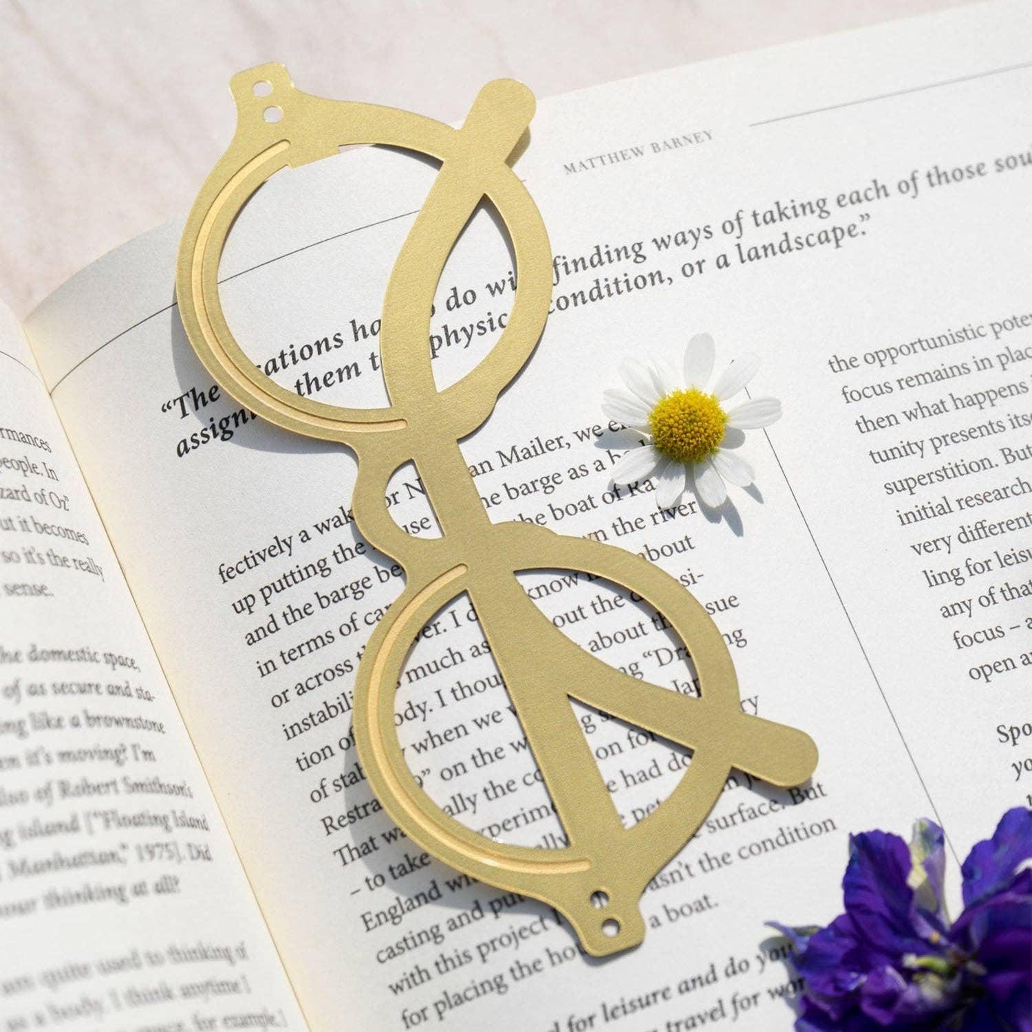 OCTAEVO The Voyage brass bookmark resting on an open book beside a daisy