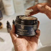 A hand lifting a fingerful of shave cream from the open jar