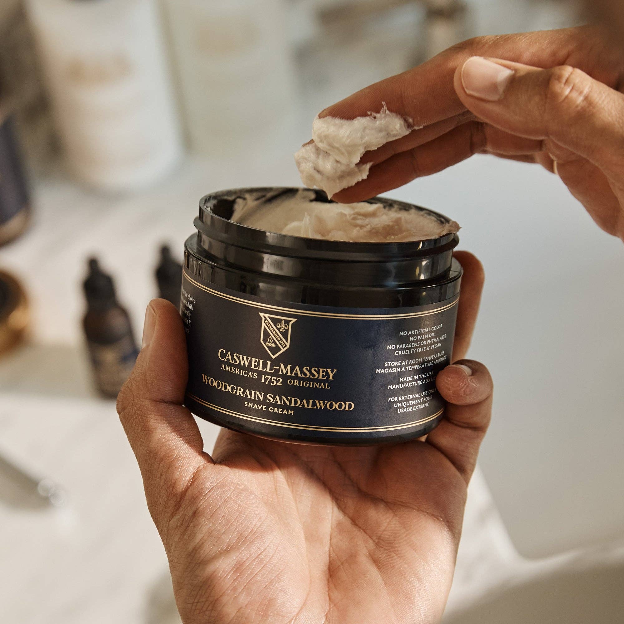 A hand lifting a fingerful of shave cream from the open jar