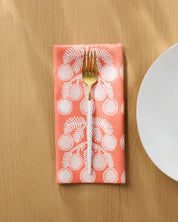 Graphic Daisies dinner napkin folded on a wooden table with a gold fork, white daisy sprigs on coral