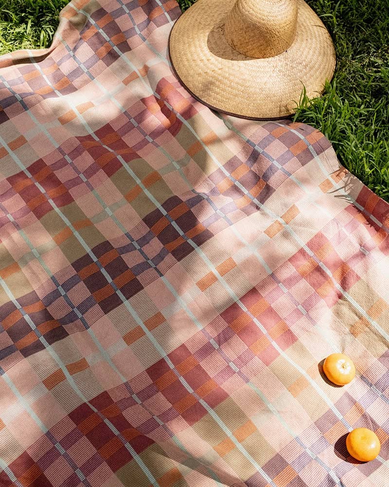 Mungo Picnic Blanket laid out on grass with a sun hat and fruit