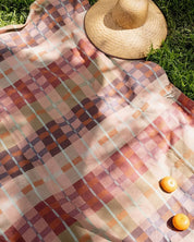 Mungo Picnic Blanket laid out on grass with a sun hat and fruit