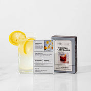 A recipe card propped beside a finished gin highball with lemon, next to the flash cards box