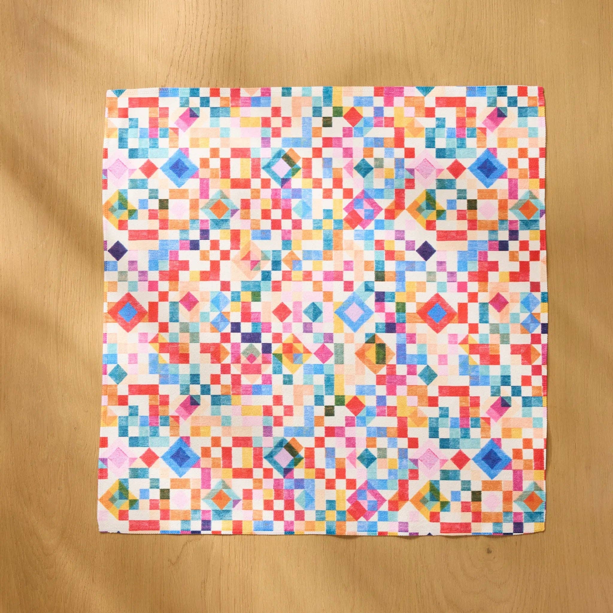 Patchwork Geo napkin opened flat on a wooden table, showing the full watercolour grid
