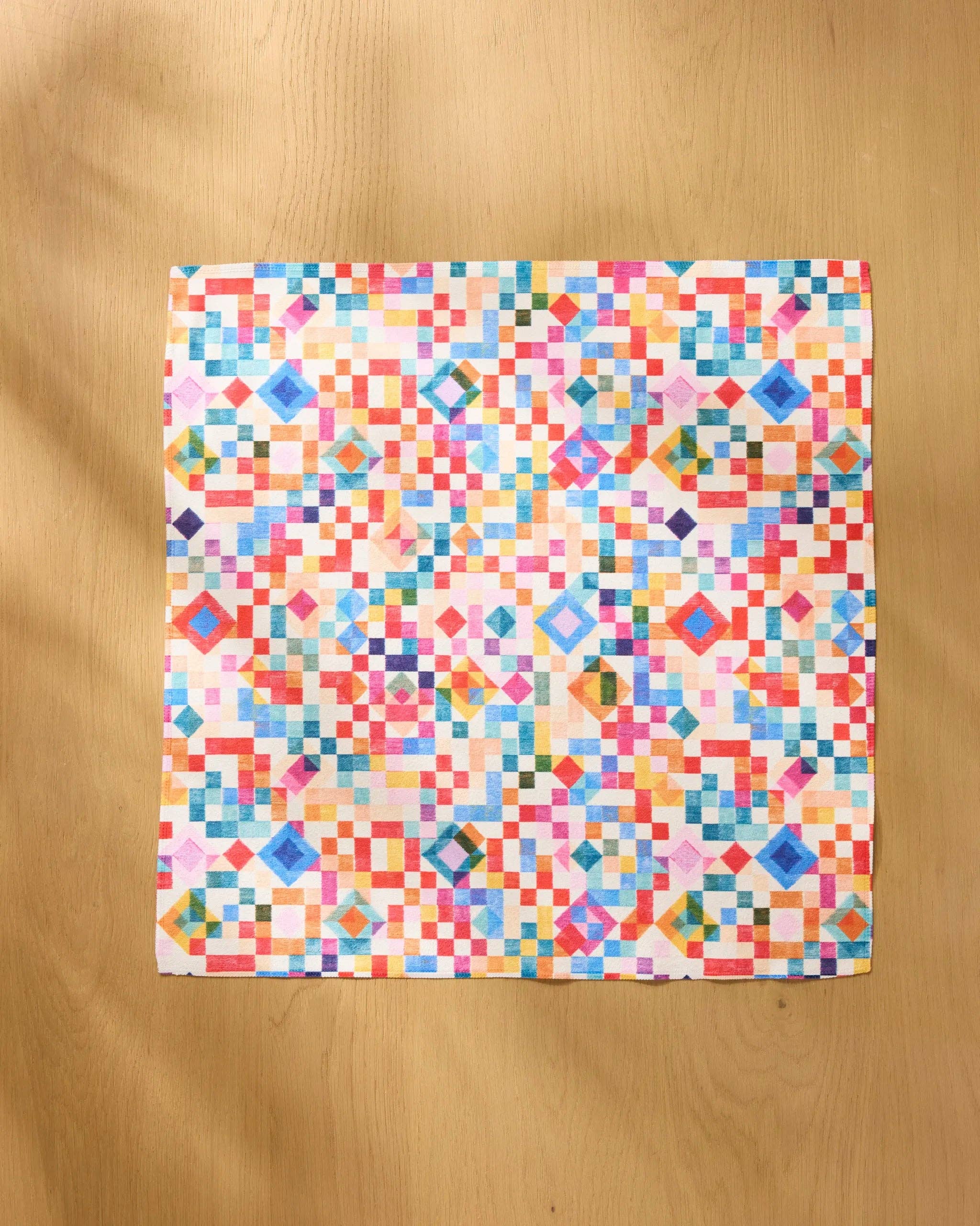Patchwork Geo napkin opened flat on a wooden table, showing the full watercolour grid