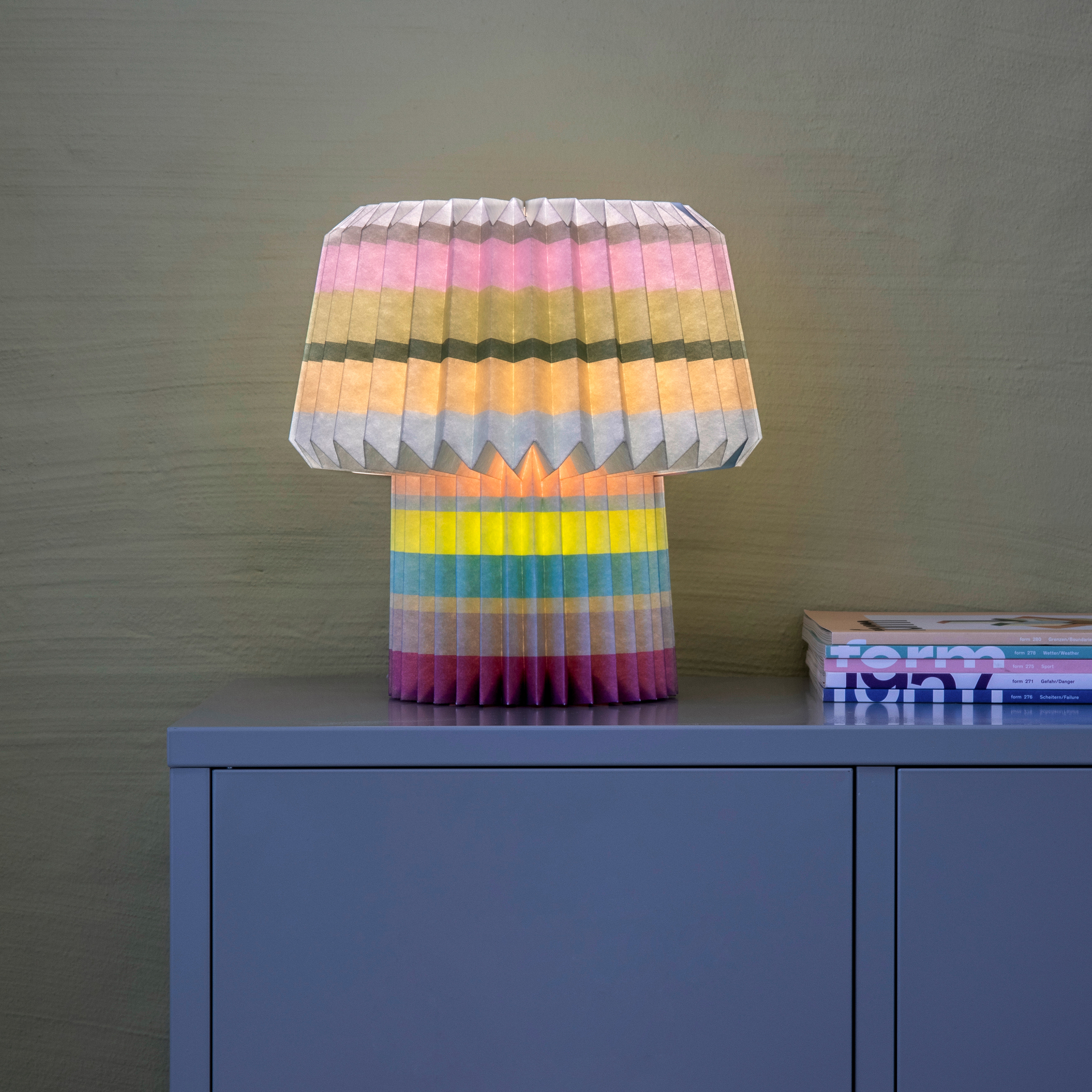 Paper Lamp Anna lit on a sideboard, casting warm ambient light through the pleated paper shade
