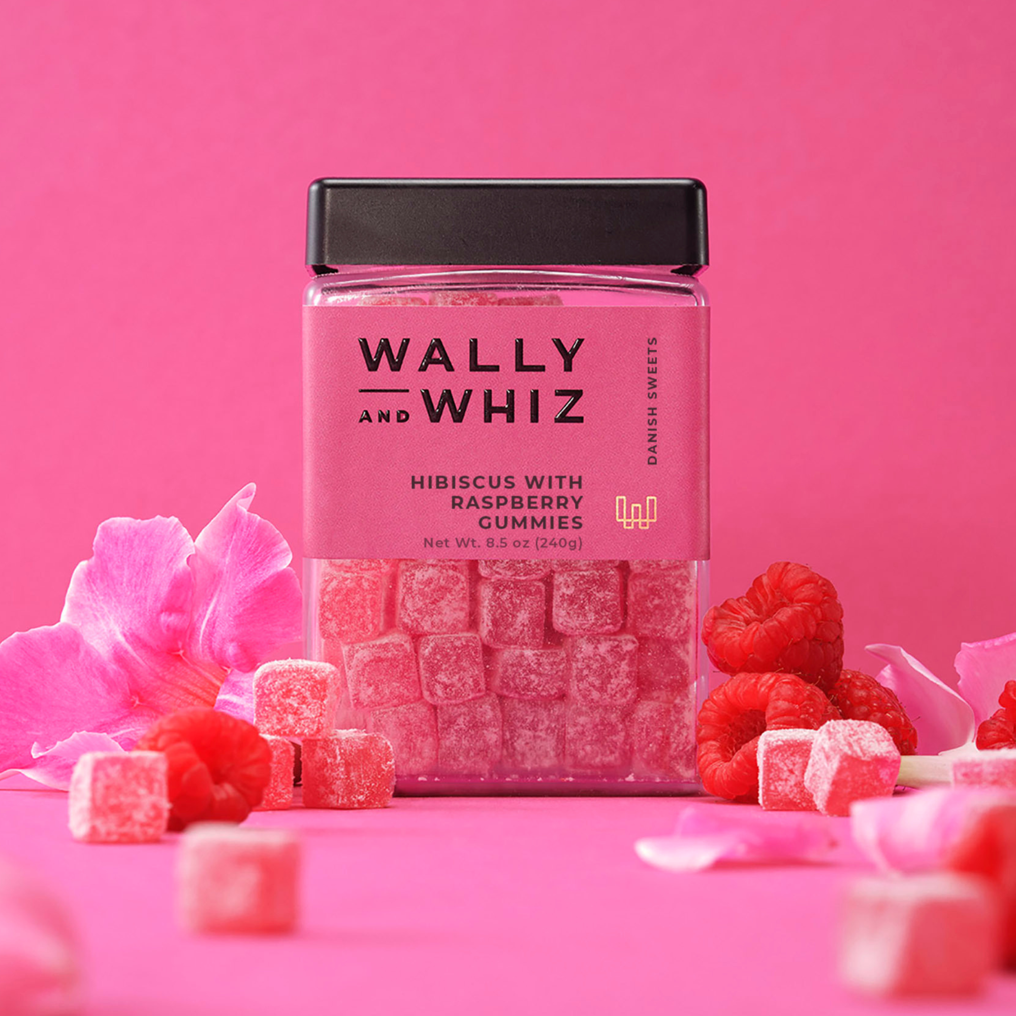 Wally and Whiz hibiscus with raspberry gummies in a pink 8.5 oz jar, surrounded by raspberries and petals