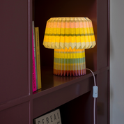 The stripes lamp lit in a burgundy bookcase, with its inline cord switch visible