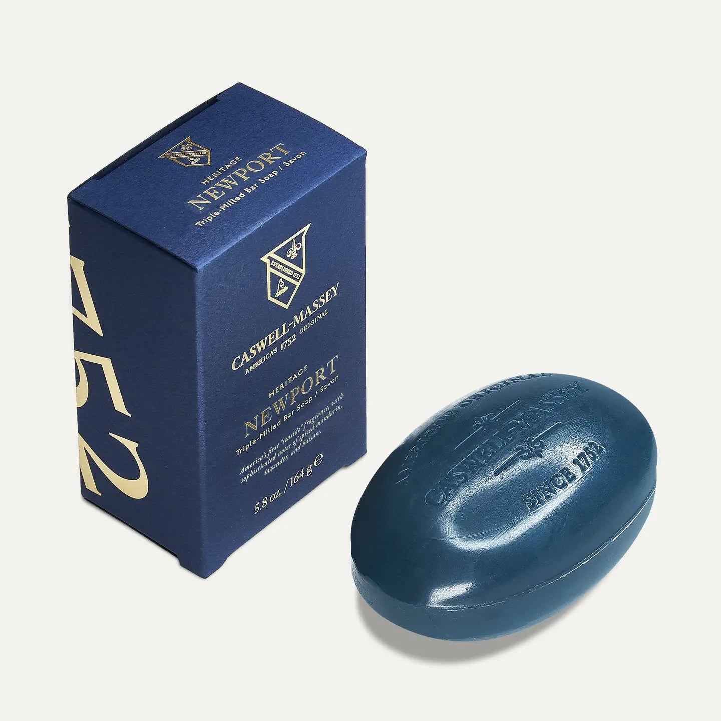 Caswell-Massey Newport bar soap, a slate blue oval bar embossed with the crest, beside its navy and gold box
