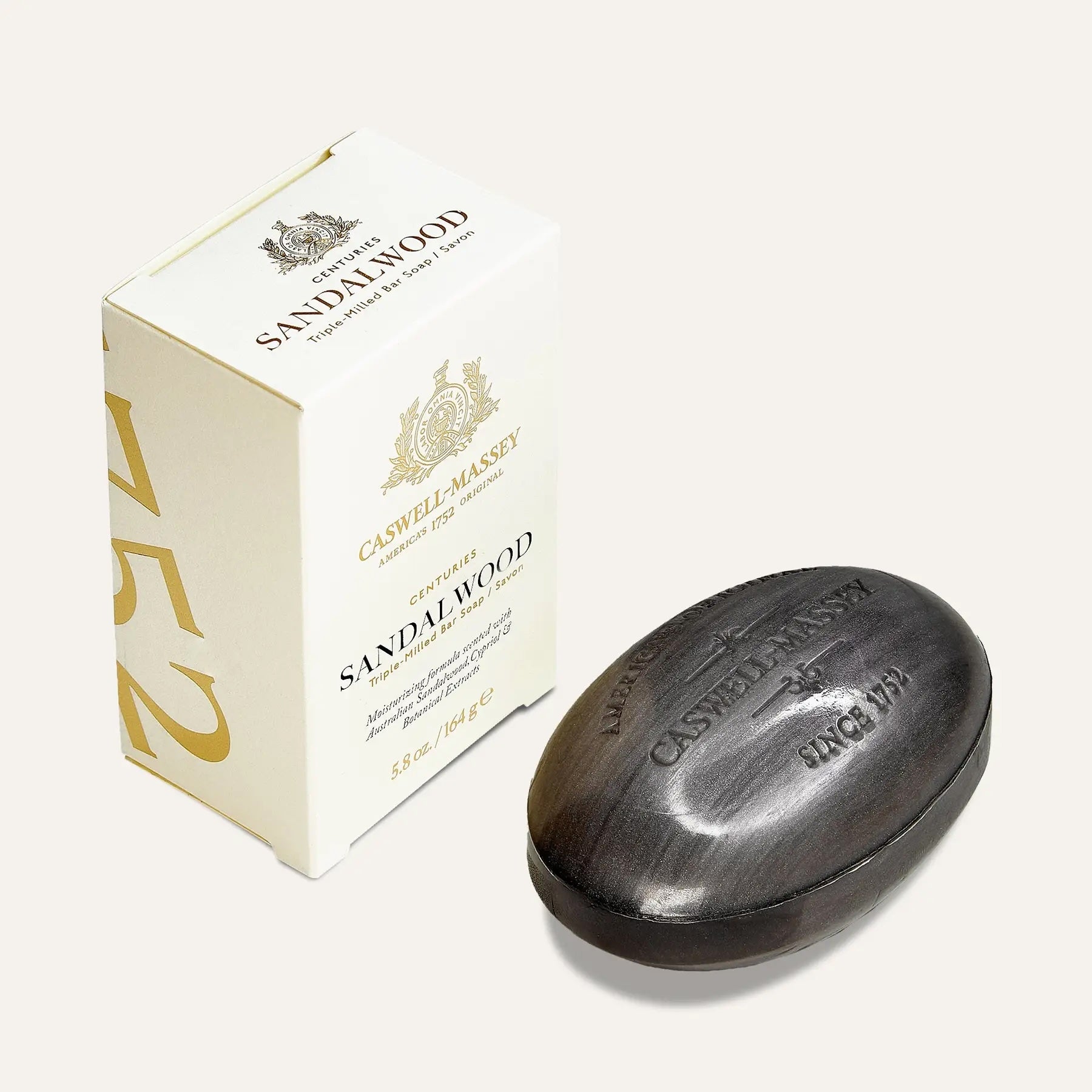 Caswell-Massey Sandalwood bar soap, a dark charcoal oval bar embossed with the crest, beside its cream and gold box