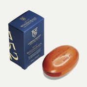 Caswell-Massey Woodgrain Sandalwood bar soap, a russet brown oval bar embossed with the crest, beside its navy and gold box