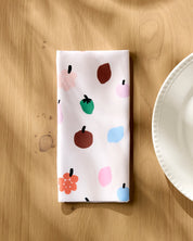 Fruit Basket napkin folded on a wooden table beside a white plate