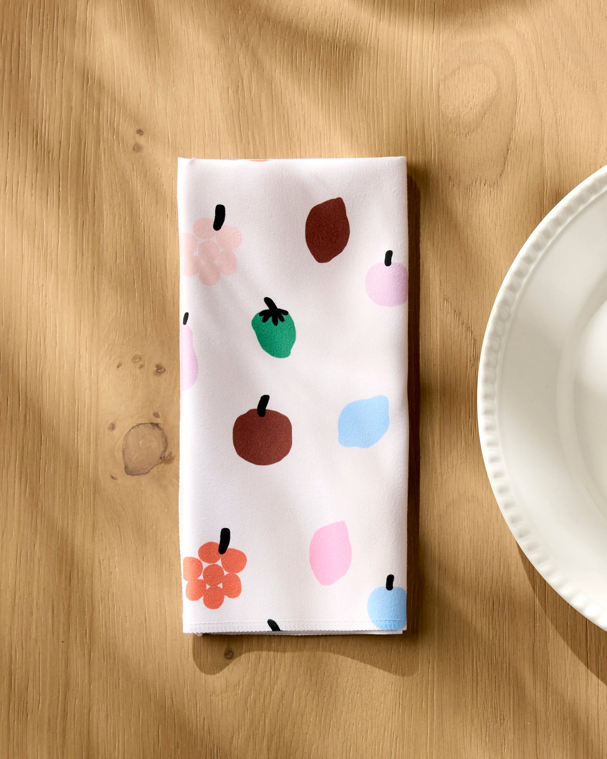 Fruit Basket napkin folded on a wooden table beside a white plate