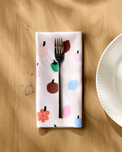Fruit Basket napkin folded on a wooden table with a fork resting on top, beside a white plate
