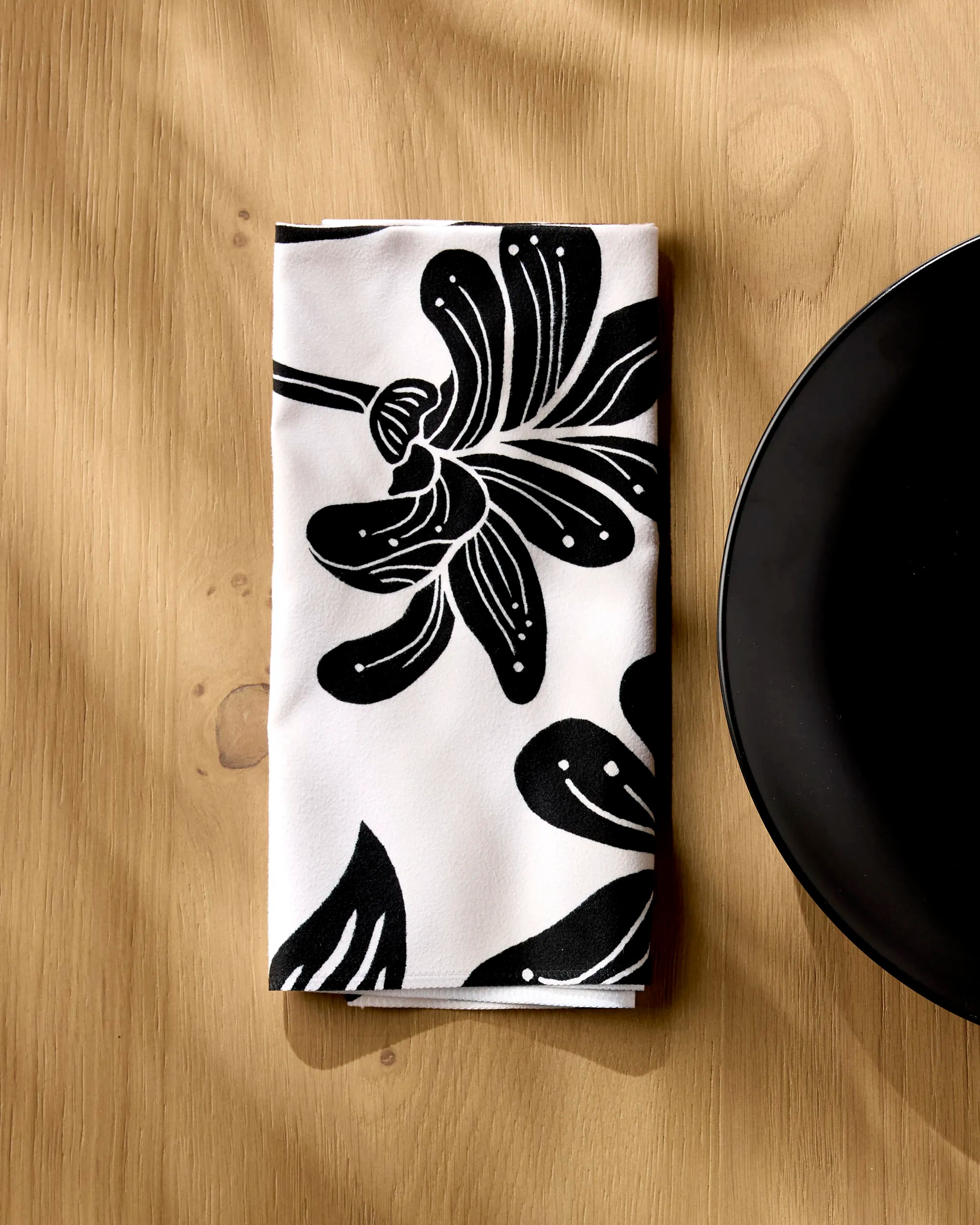 Giant Lush Floral napkin folded on a wooden table beside a white plate