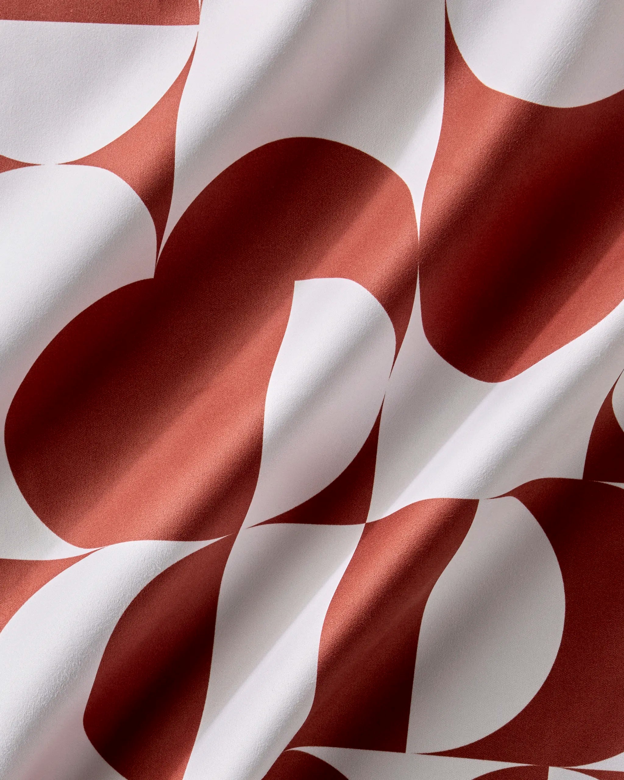Close-up of the Circle Playground print, rust red and white curves and semicircles on draped fabric