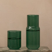 Forest green carafe and matching stackable glass filled with water on a marble surface