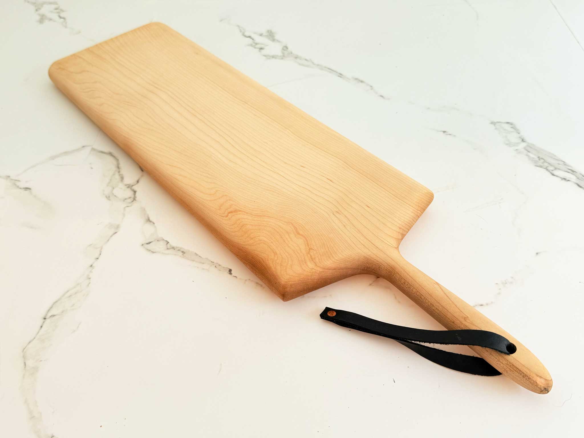 KHEM Studios Monster Board in Maple, a long handled serving board with a leather hanging strap