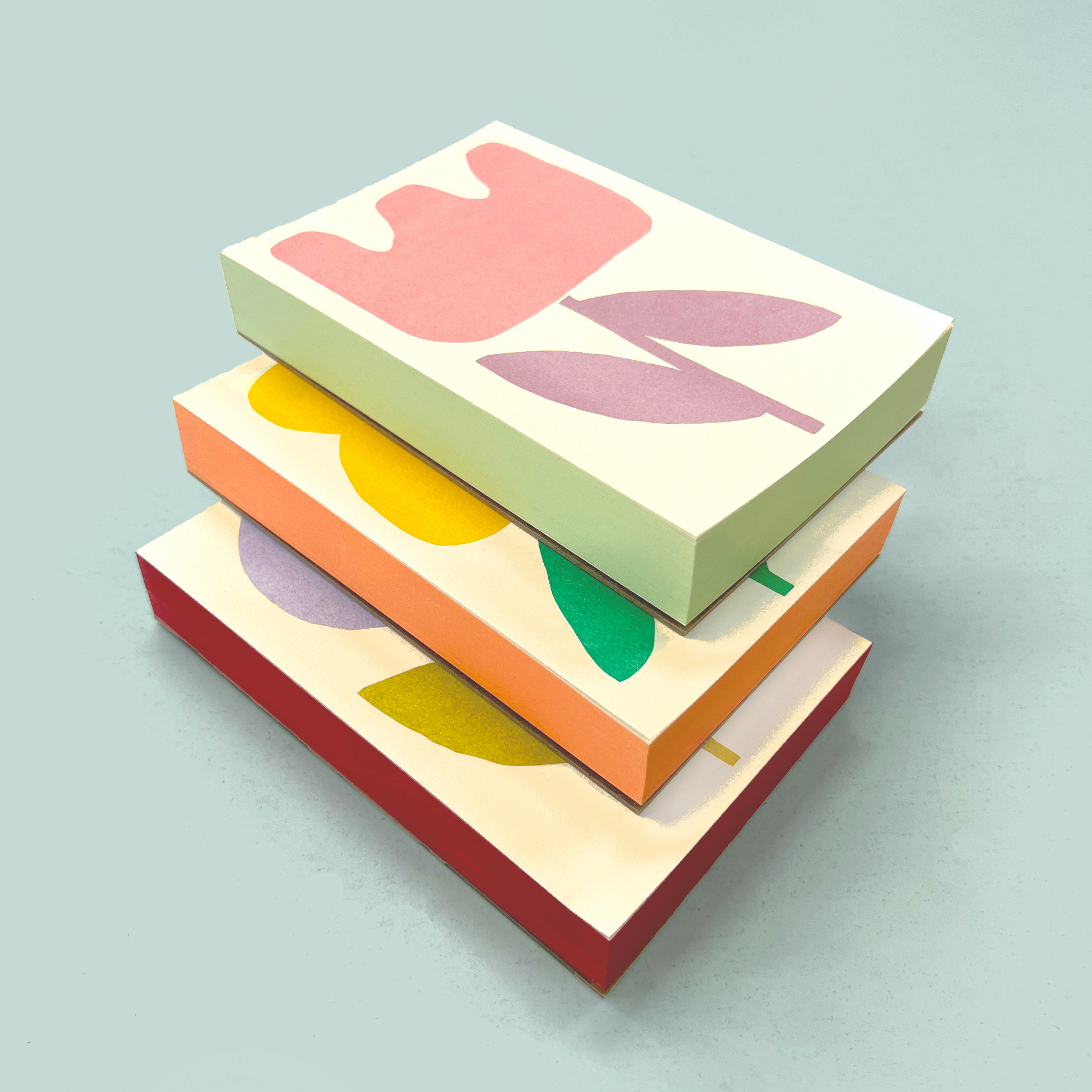 Three flower pads stacked, showing the hand-painted edges in green, orange and red