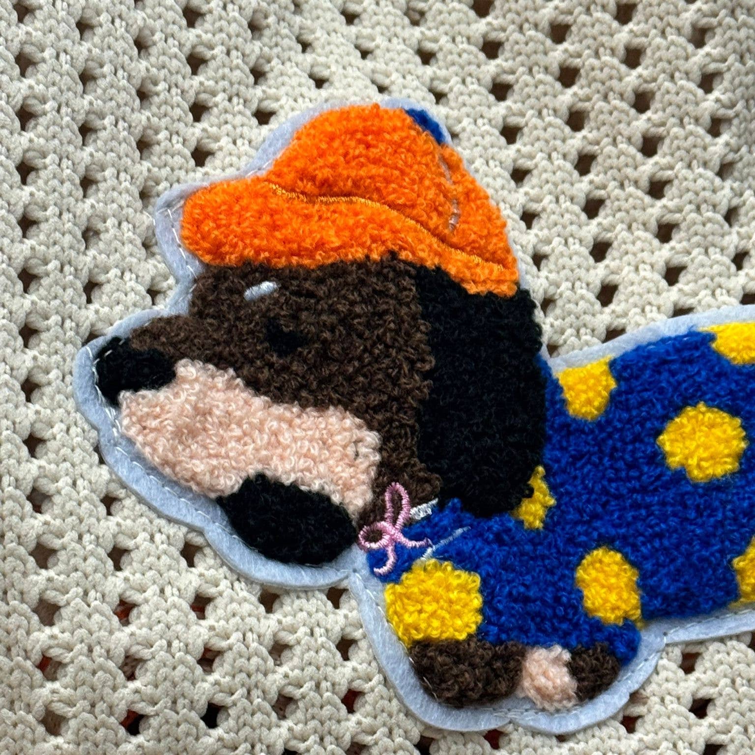 Close-up of the embroidered dachshund patch, wearing an orange rain hat and a blue coat with yellow spots