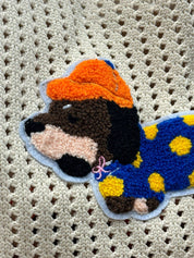 Close-up of the embroidered dachshund patch, wearing an orange rain hat and a blue coat with yellow spots