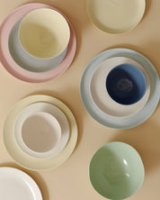 Mud Australia dinner plates and bowls stacked as place settings in pink, yellow, blue and cream, shot from above