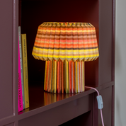 The loops lamp lit on a burgundy bookshelf beside upright books, glowing orange and yellow