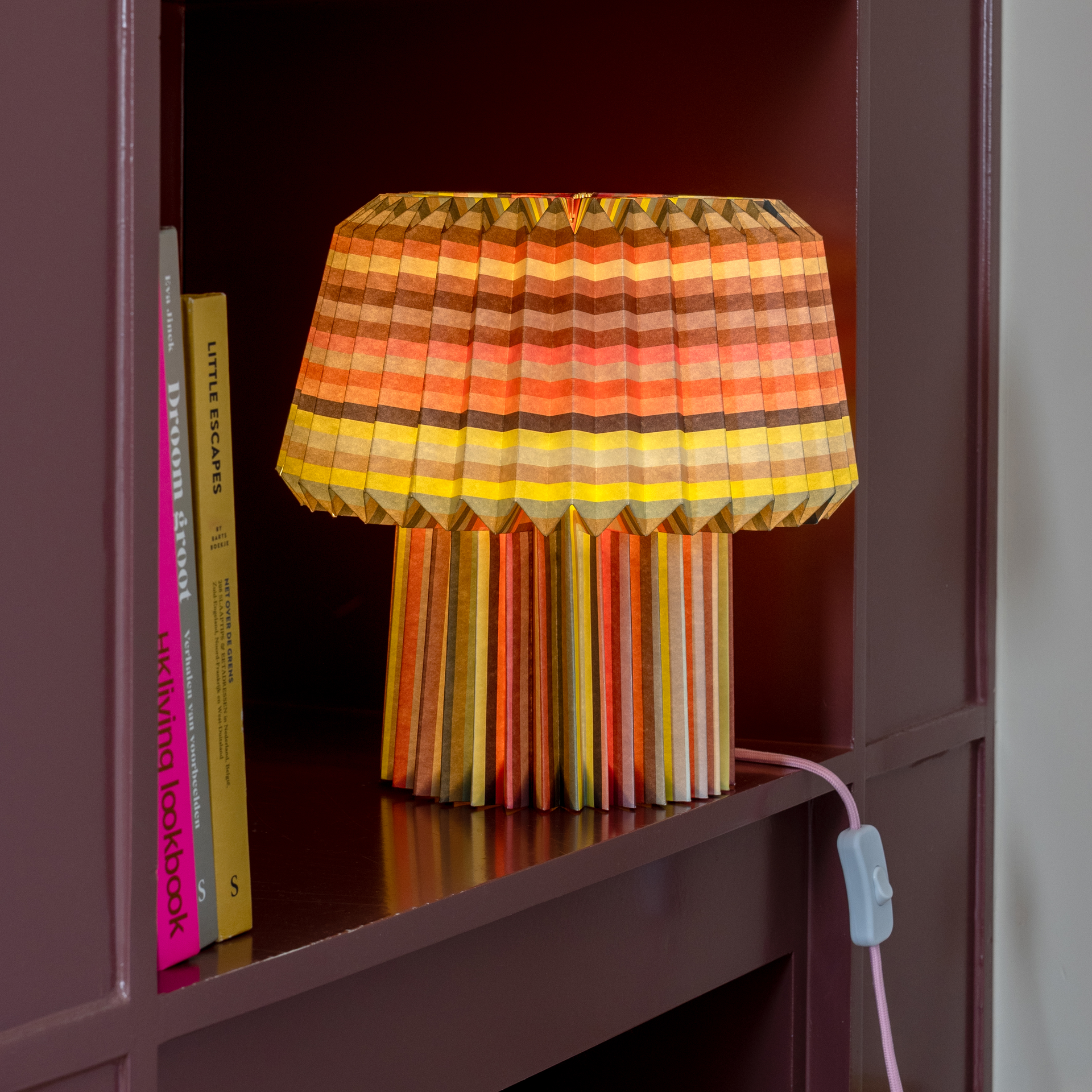 The loops lamp lit on a burgundy bookshelf beside upright books, glowing orange and yellow