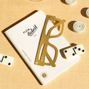 OCTAEVO Plein Soleil brass bookmark resting on a Cinema Notes notebook with dominoes
