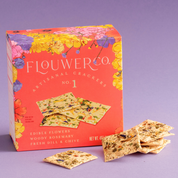 Flouwer Co. No. 1 crackers in a coral floral box with herb and flower flecked crackers stacked beside it