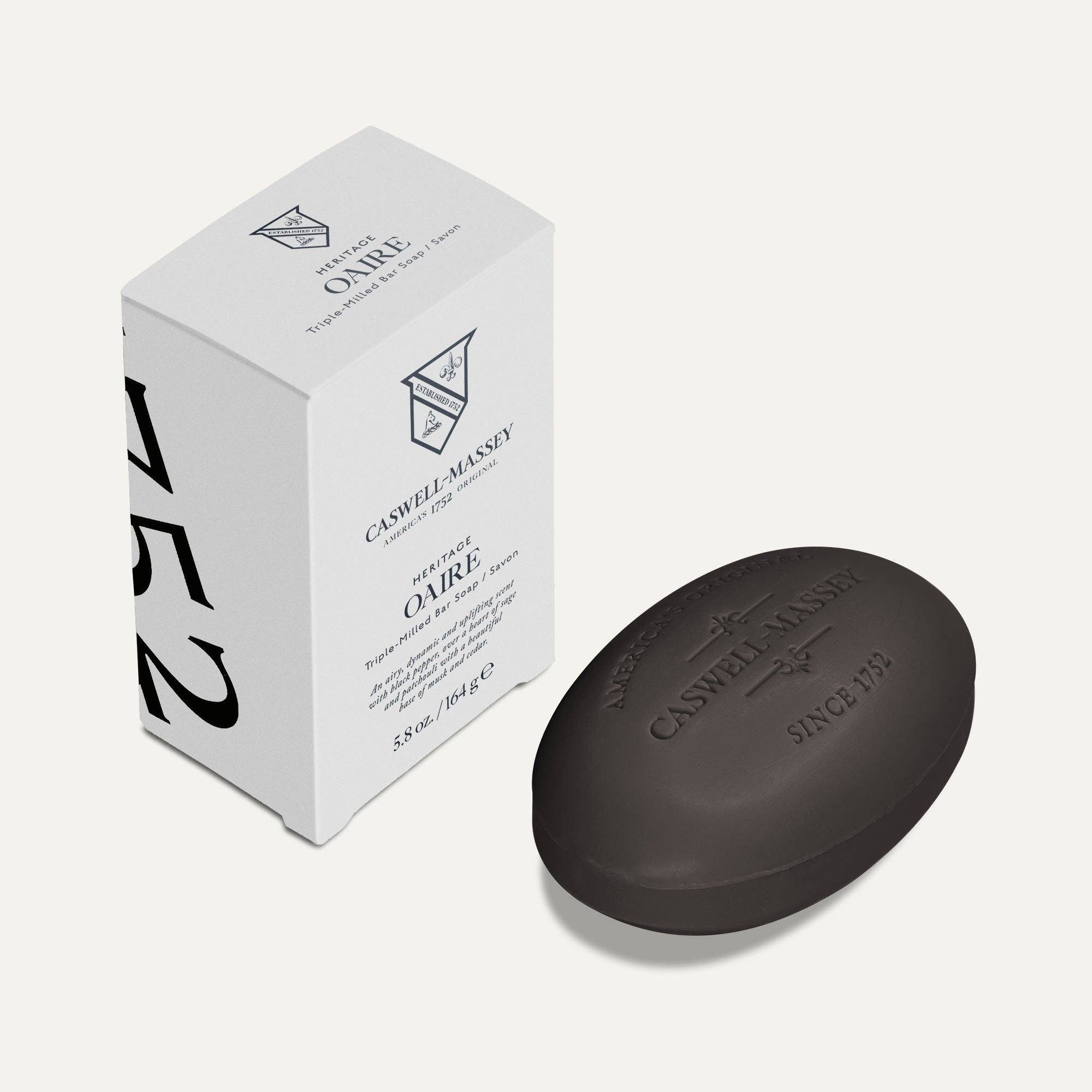 Caswell-Massey Oaire bar soap, a dark charcoal brown oval bar embossed with the crest, beside its white box with black lettering